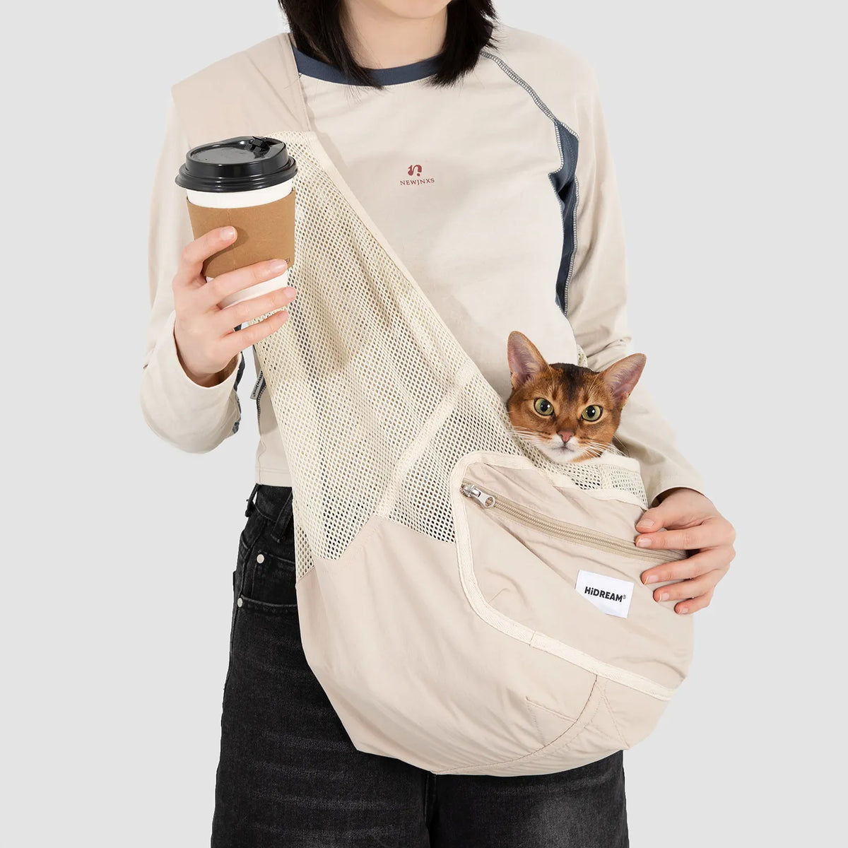 Person carrying a cat in the Milk Brown mesh pet sling, showing its mesh body and zipped side pocket