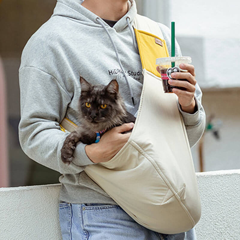 Persona con un gatto in una borsa beige dalla larga tracolla gialla