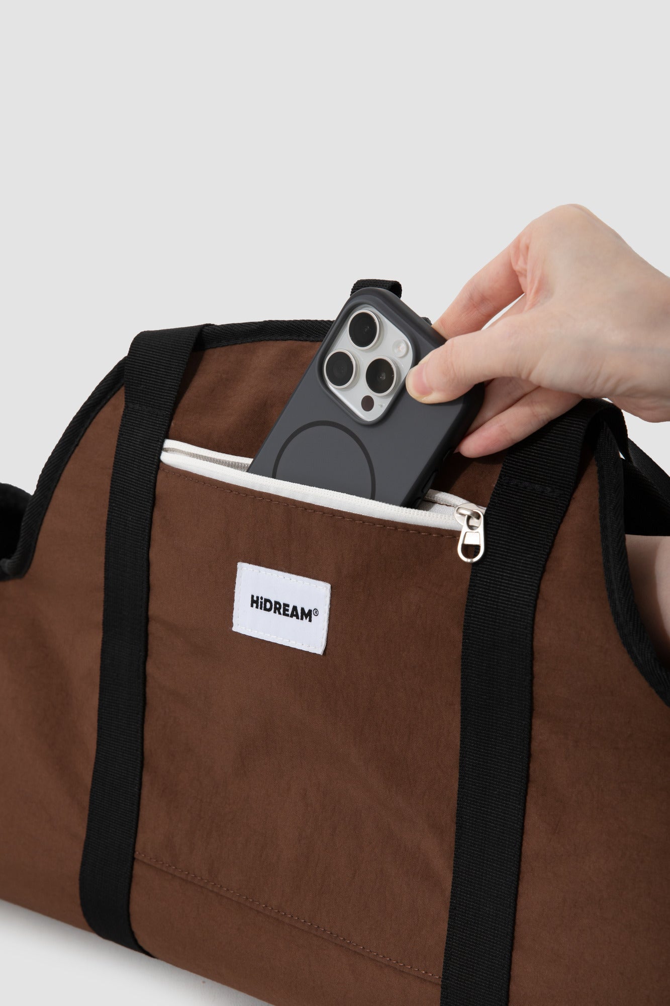 Close-up of the brown carrier's zipped front storage pocket with a phone for scale.