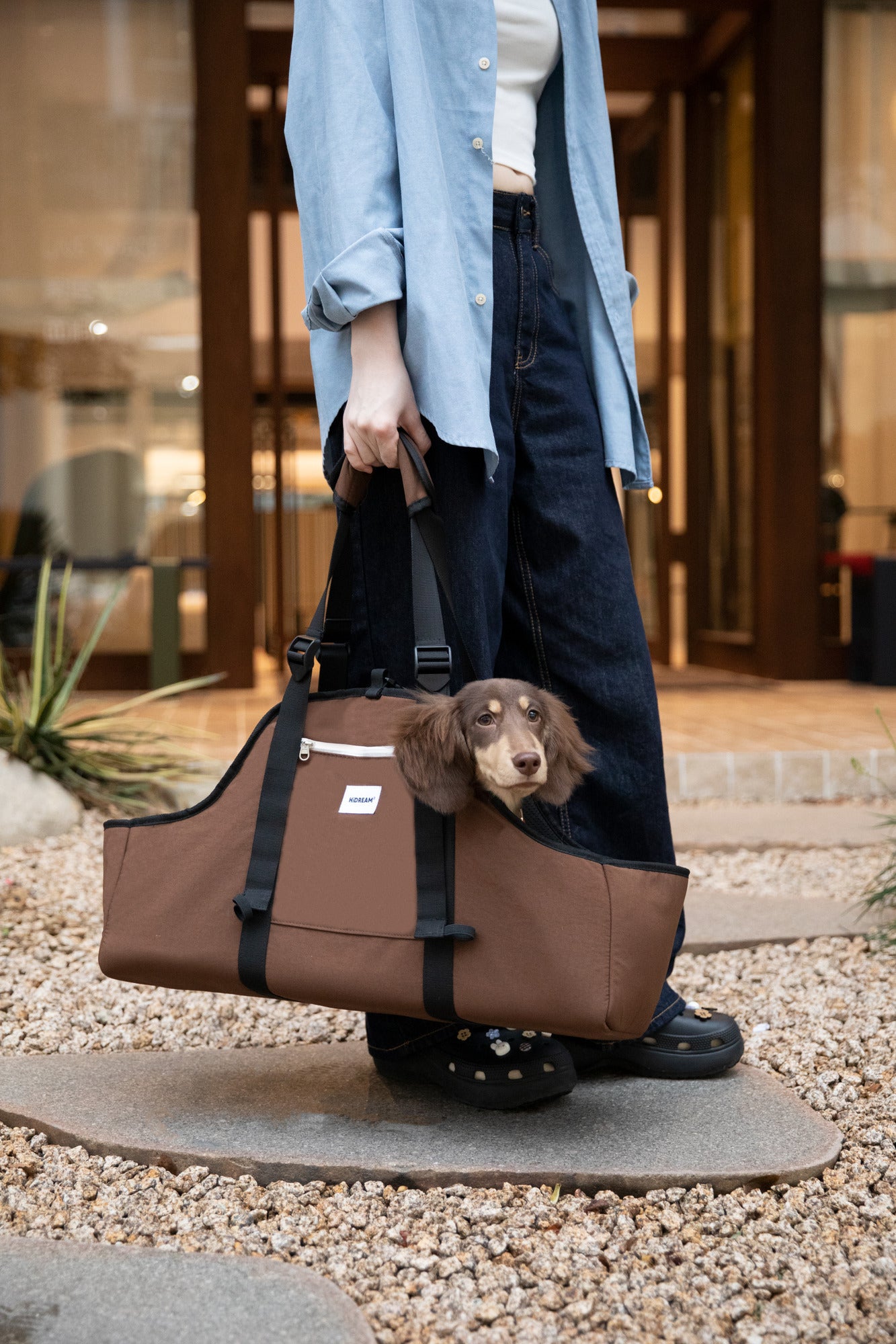 Brown dog carrier held by its handles during an outdoor outing.