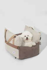 Small white dog resting in the brown and cream pet bed in a studio setting.